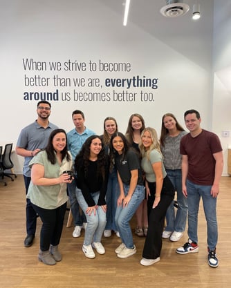 A group of Populus Group Arizona employees smiling together in front of an office wall that reads, “When we strive to become better than we are, everything around us becomes better too.”