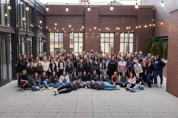 A large group of Populus Group employees gathered for a team photo at Climber Summit 2025 in an outdoor courtyard with string lights overhead.
