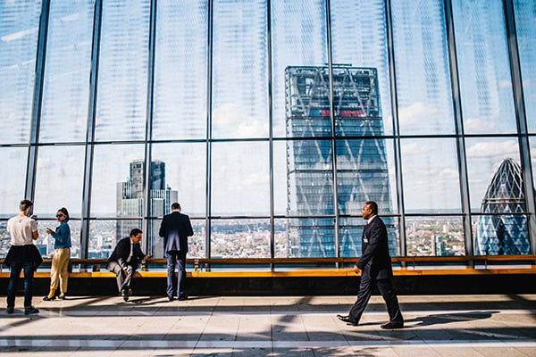 A man walking down a hallway with large windows overlooking a city skyline.