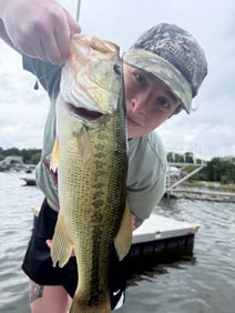 Remy holds a large bass by the mouth with a body of water behind her.