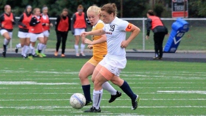 Remy dribbles a soccer ball in front of an opponent on the soccer field.