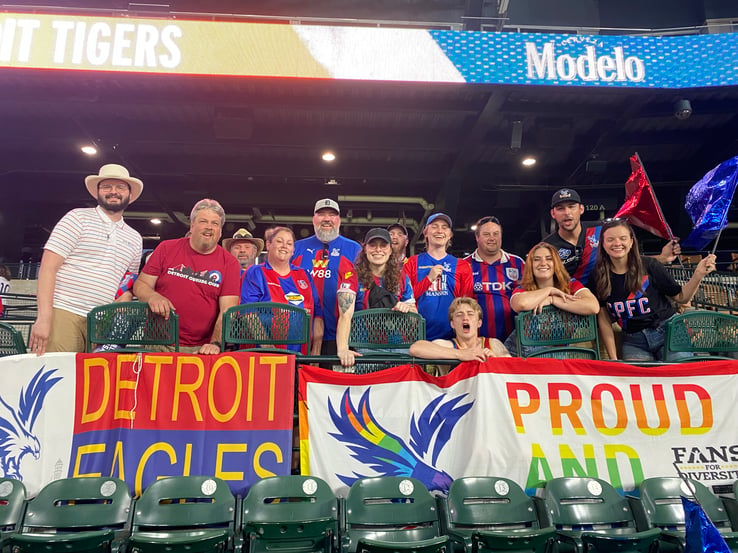 Remy stands among a large group with banners that say 'Detroit Eagles' and 'Proud'.