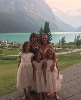 JoAnna and Renee smile with three young girls in front of a mountain background.