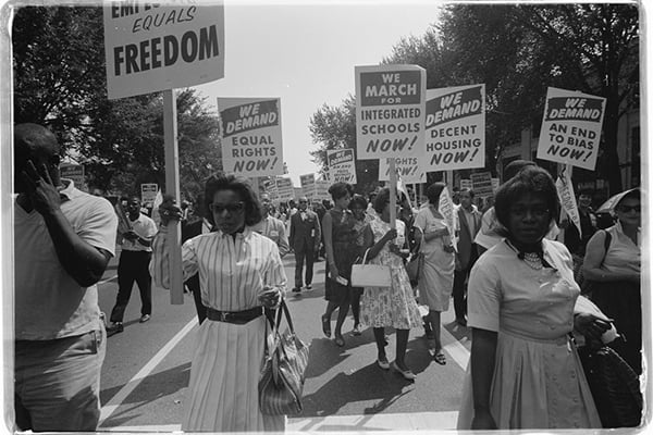 A procession of African Americans holding signs for equal freedoms, rights, housing, and schools during the March on Washington in 1963.