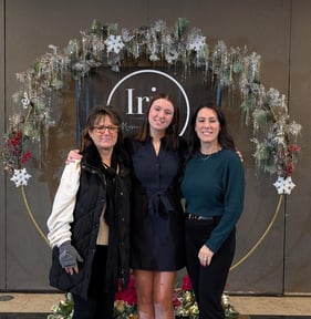 JoAnna and Renee smile with another woman between them in front of a holiday wreath.