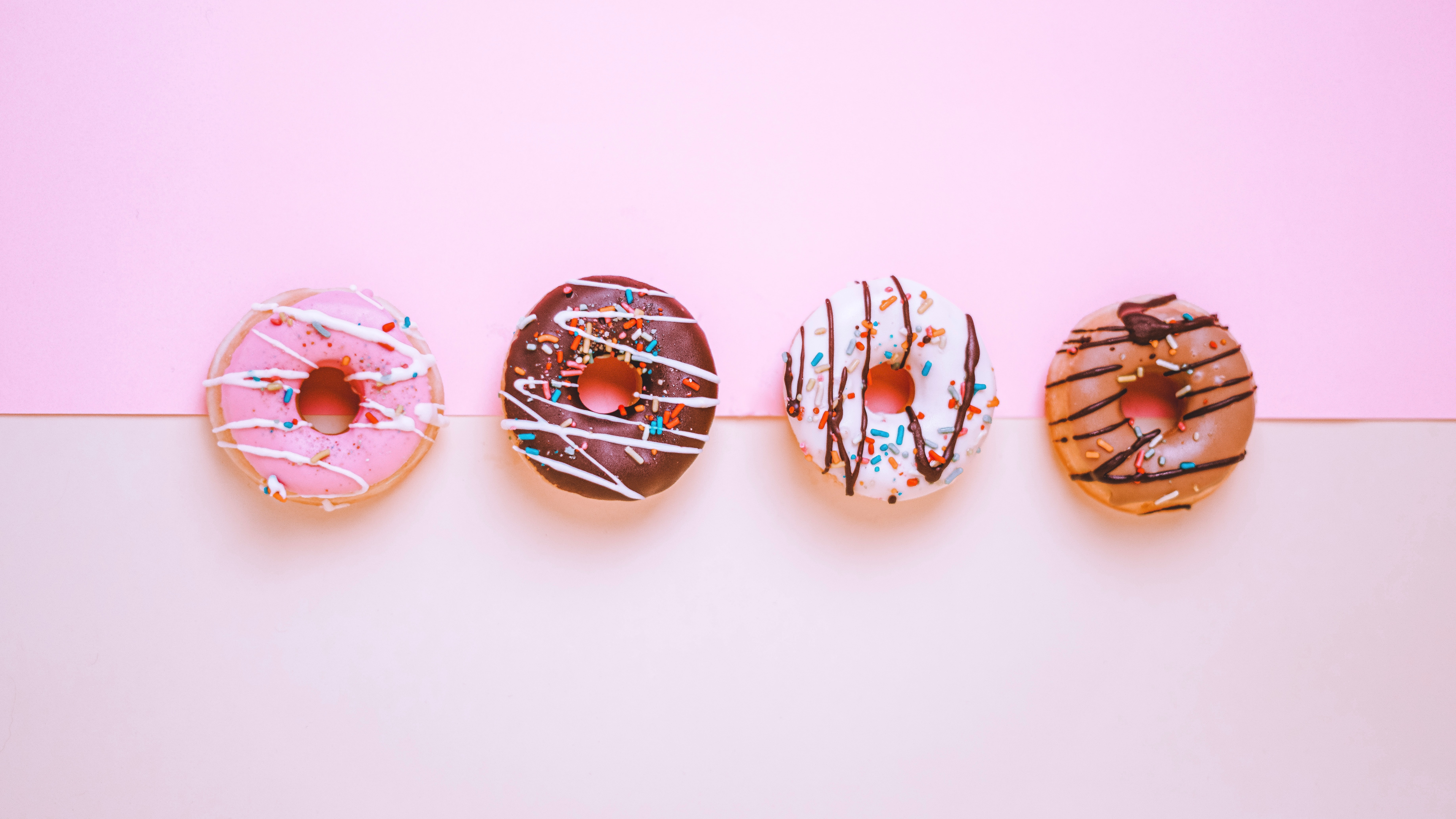 A pink background boasts four deliciously decorated doughnuts.